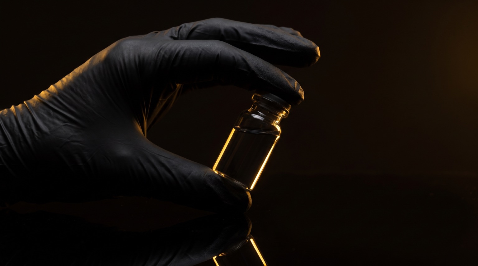 Mano con guante negro inspeccionando un vial a contraluz dorada
